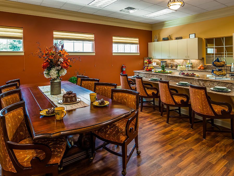A warm and inviting dining room with a wooden table, chairs, and decorative elements, featuring a kitchen area in the background.