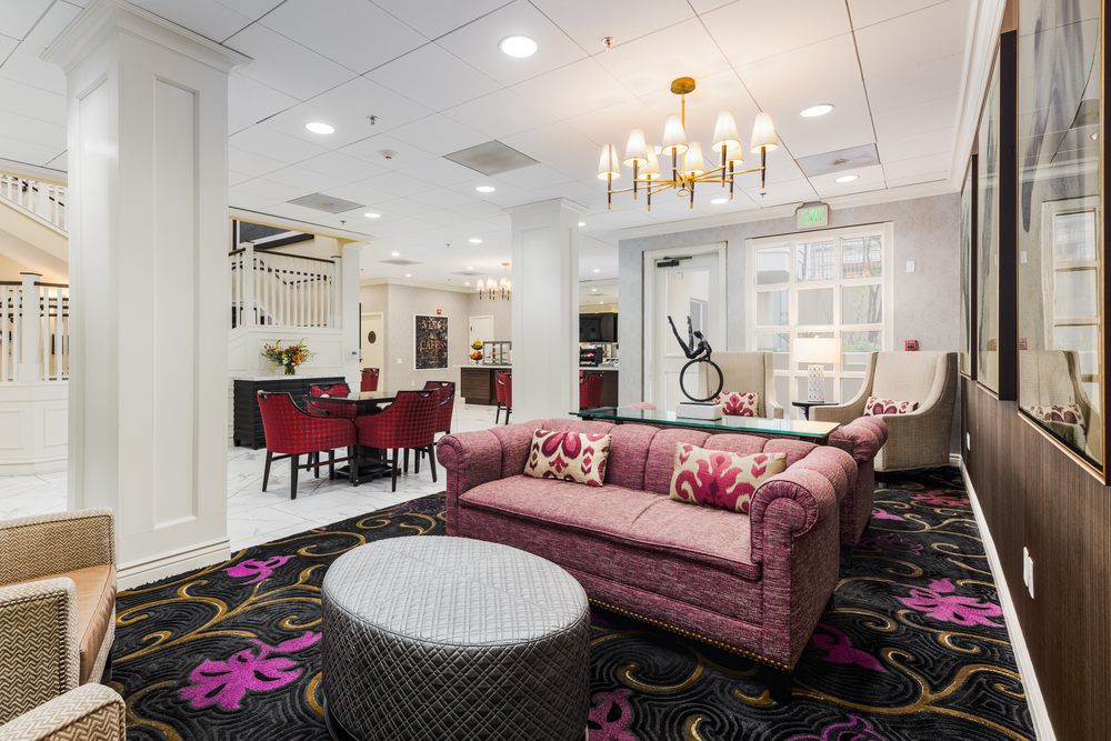 A stylish and modern living room featuring a pink sofa, elegant chandelier, and vibrant carpet.