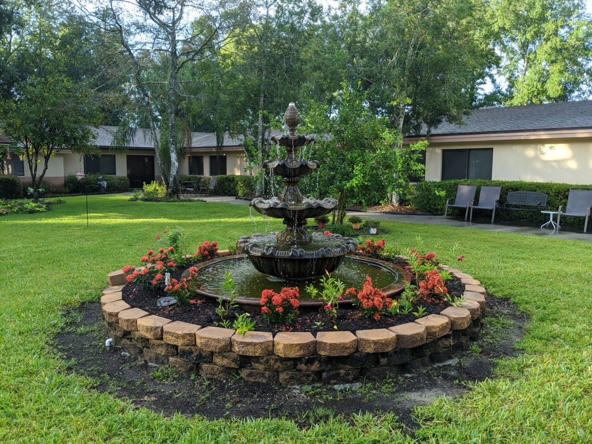 A beautiful garden with a multi-tiered fountain surrounded by vibrant flowers and greenery.
