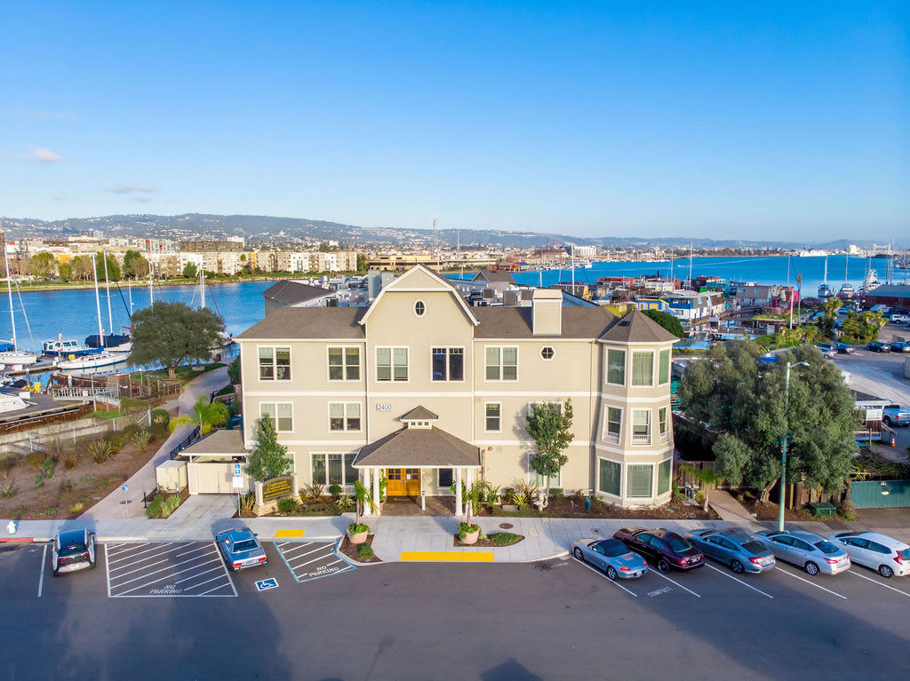 Aerial view of a waterfront building with nearby parking and harbor scenery.