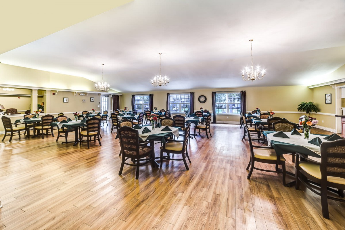 A spacious dining room with elegantly arranged tables and chairs, featuring wood flooring and chandeliers.