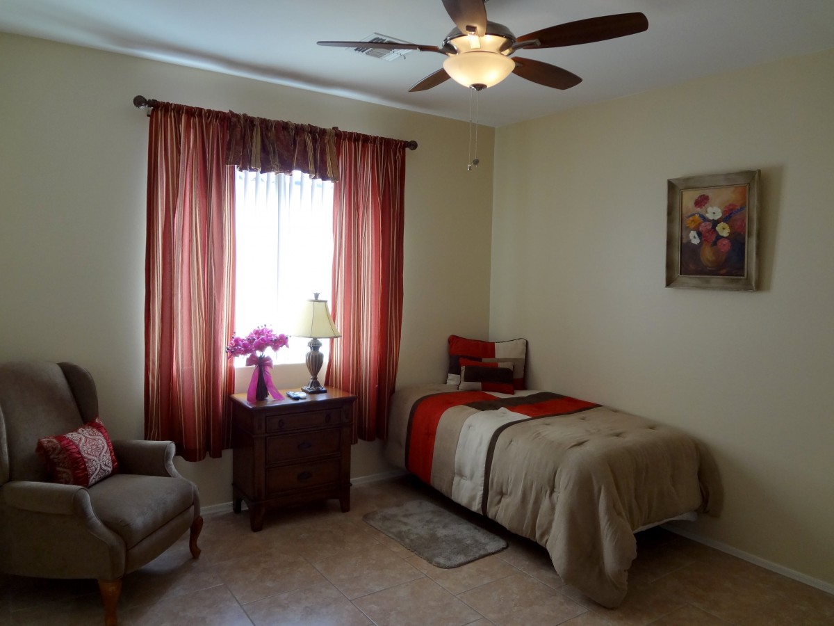 A cozy bedroom with a single bed, rust-colored curtains, and a ceiling fan.