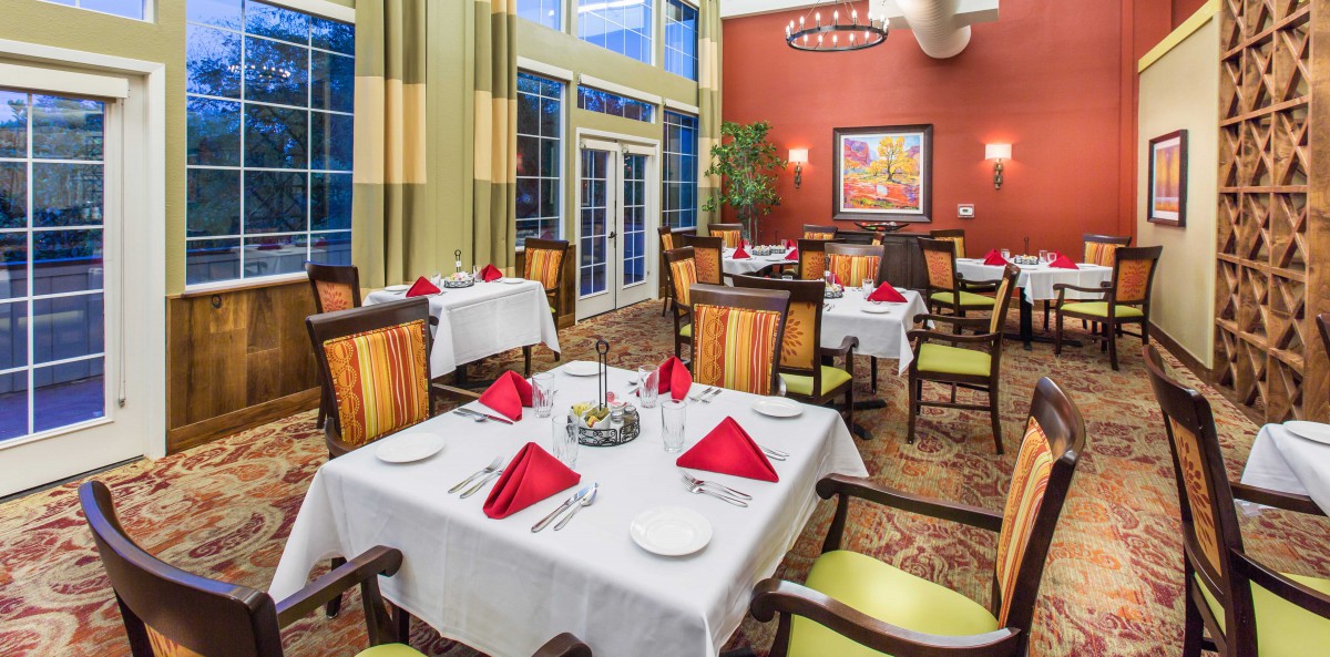 Elegant dining area with tables set for guests, featuring red napkins and comfortable seating.