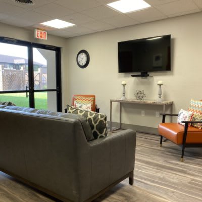 A modern living room with a sofa, chairs, and a wall-mounted TV.