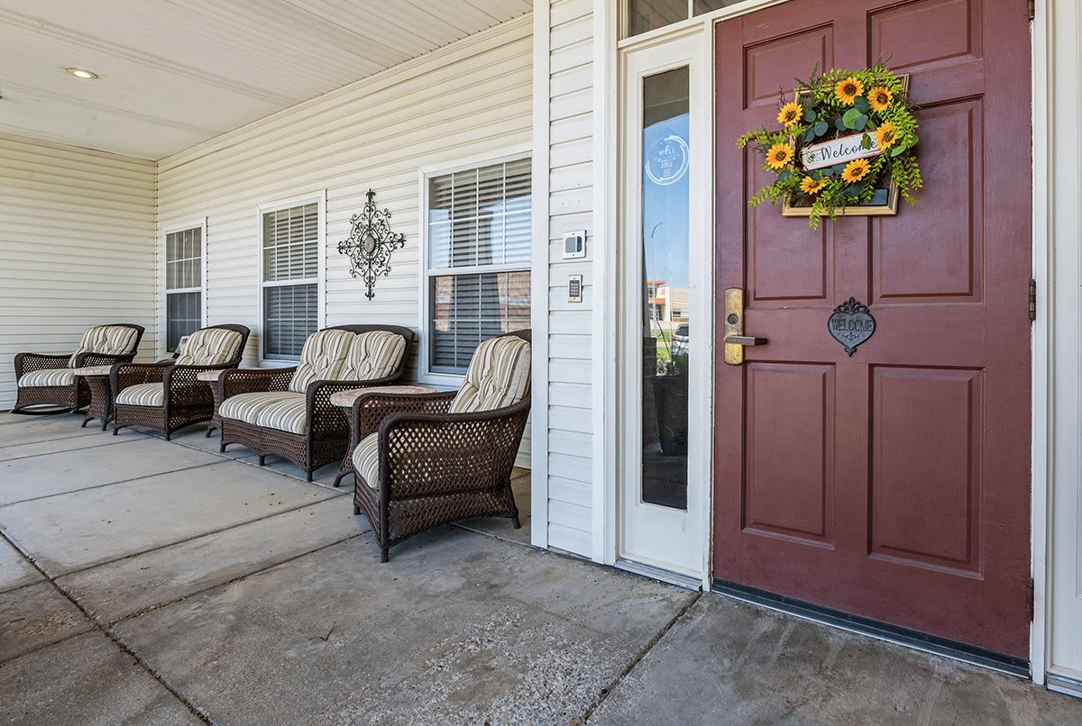 A welcoming front porch with wicker chairs and a sunflower wreath on a red door.