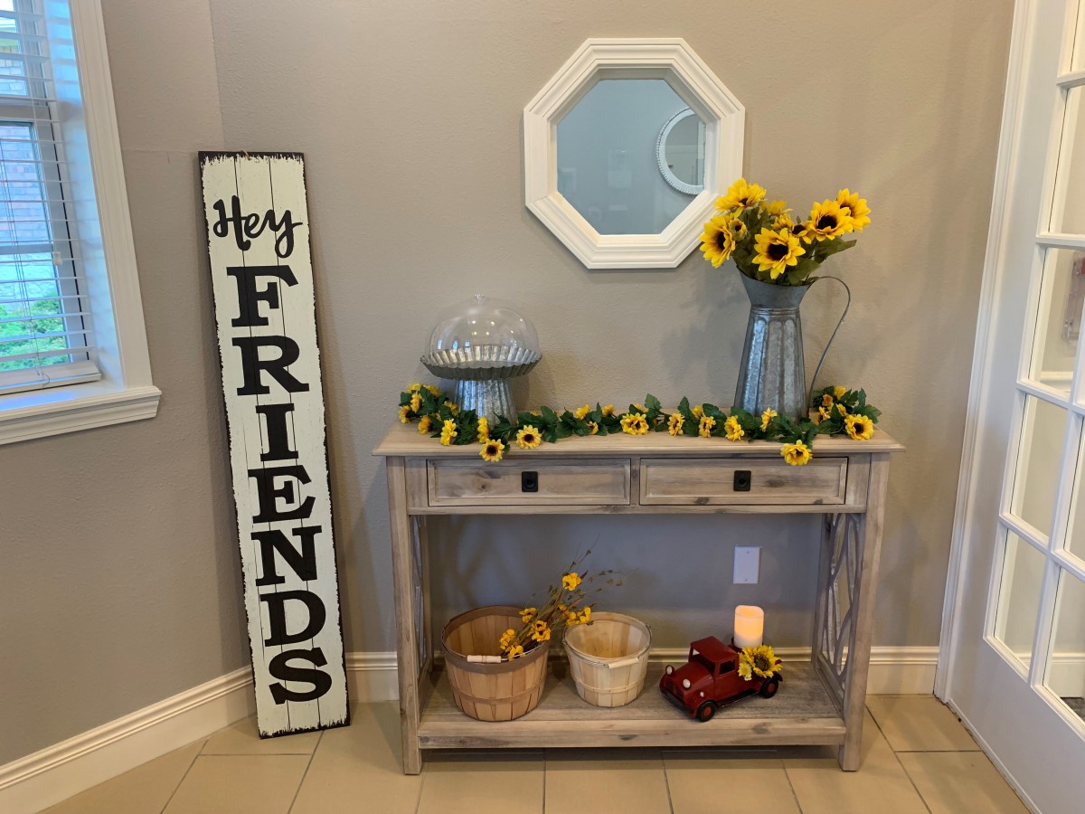 A welcoming entryway with a sunflower-themed decor, featuring a console table, a large 'Hey FRIENDS' sign, and a wall mirror.