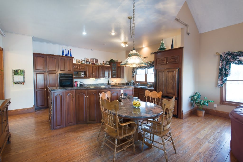 A spacious kitchen with wooden cabinets, a dining table with chairs, pendant lighting, and hardwood flooring.