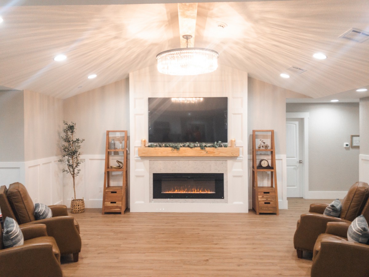 A modern living room with a cozy fireplace and mounted TV, featuring minimalist decor and wood flooring.