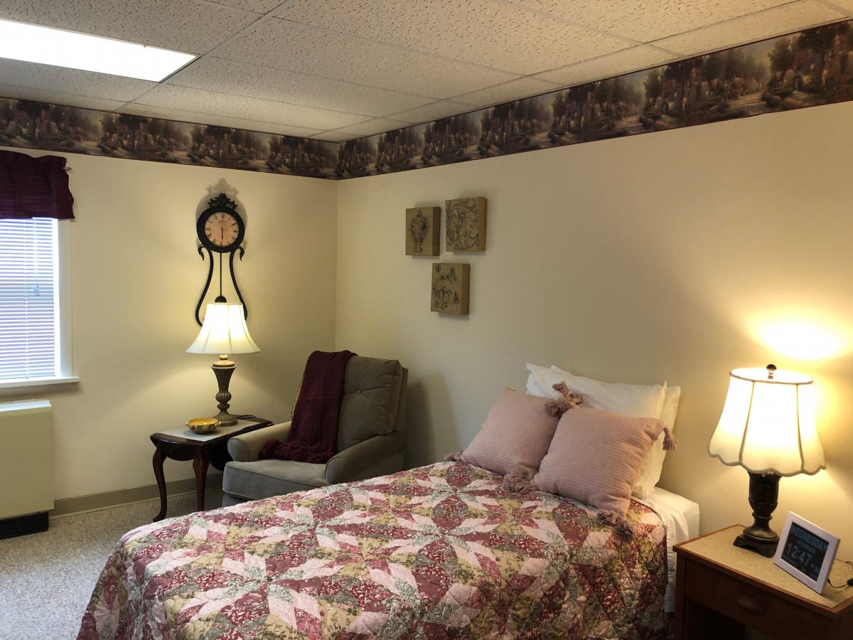 A cozy bedroom featuring a bed with patterned bedding, a comfortable chair, and ambient lighting.