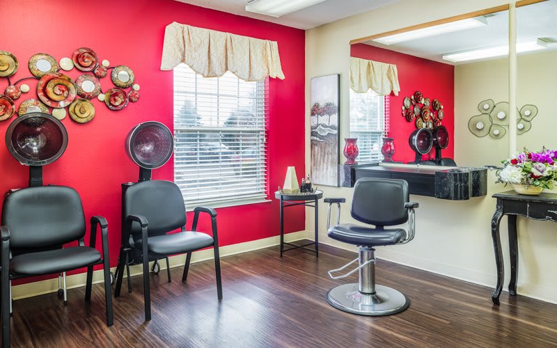 A well-lit hair salon interior with red walls, featuring styling chairs and a large mirror.
