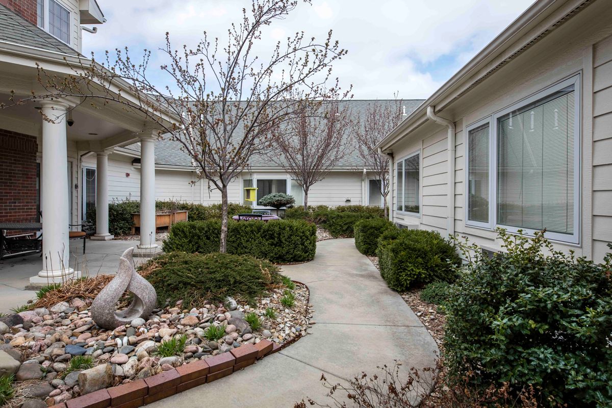 A serene courtyard with a pathway surrounded by neatly trimmed shrubs and residential buildings.