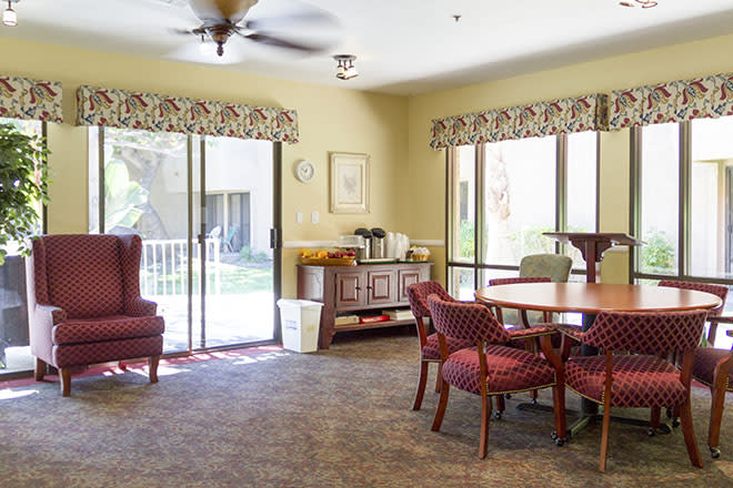 A cozy living room with a table, chairs, and large windows overlooking a garden.