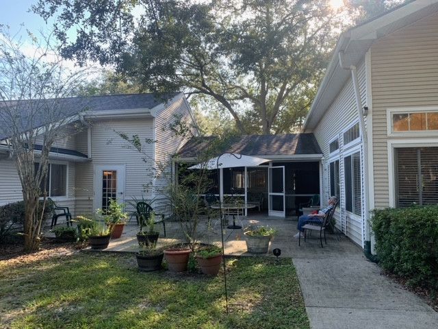 A serene backyard patio with potted plants and outdoor seating under the shade of trees.