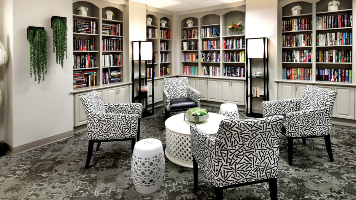 A modern library reading room with patterned armchairs and filled bookshelves.