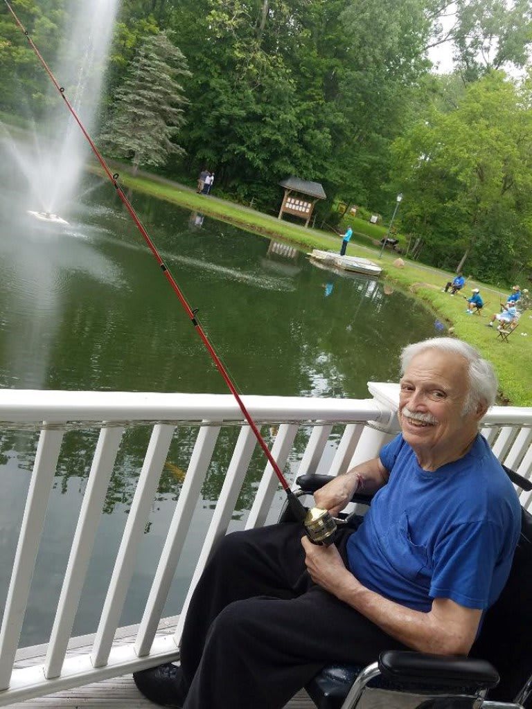 An elderly man fishing by a pond on a peaceful day.