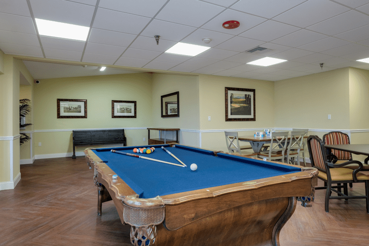 A recreation room featuring a billiard table with blue felt and surrounding seating.