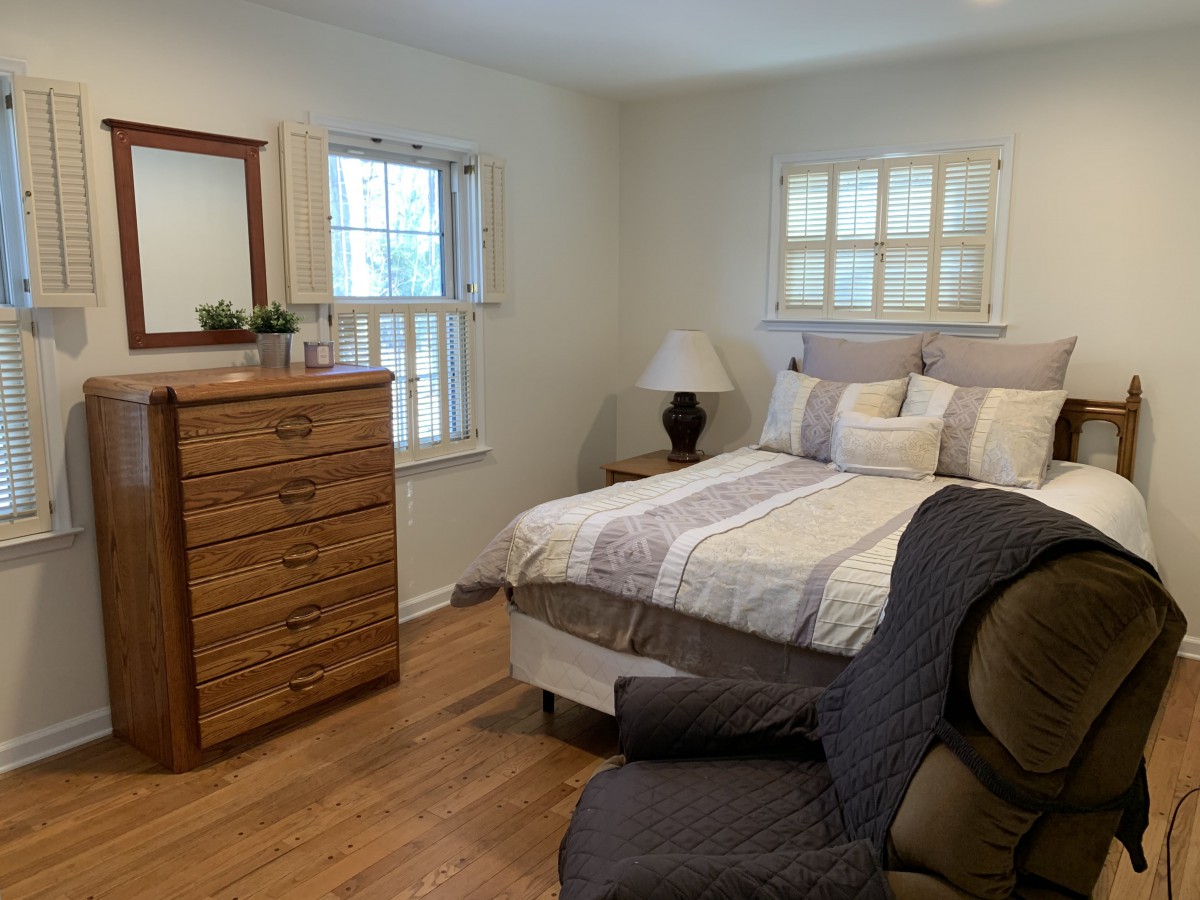 A cozy bedroom with a bed, dresser, and armchair.