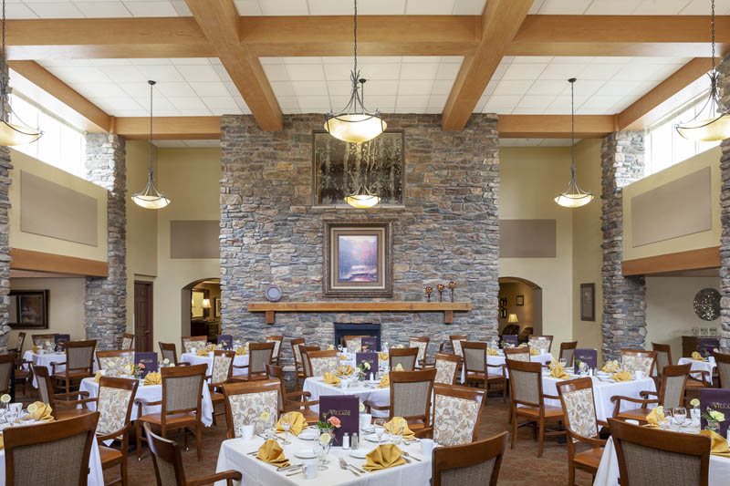 A beautifully set dining room with elegantly arranged tables and a stone fireplace.