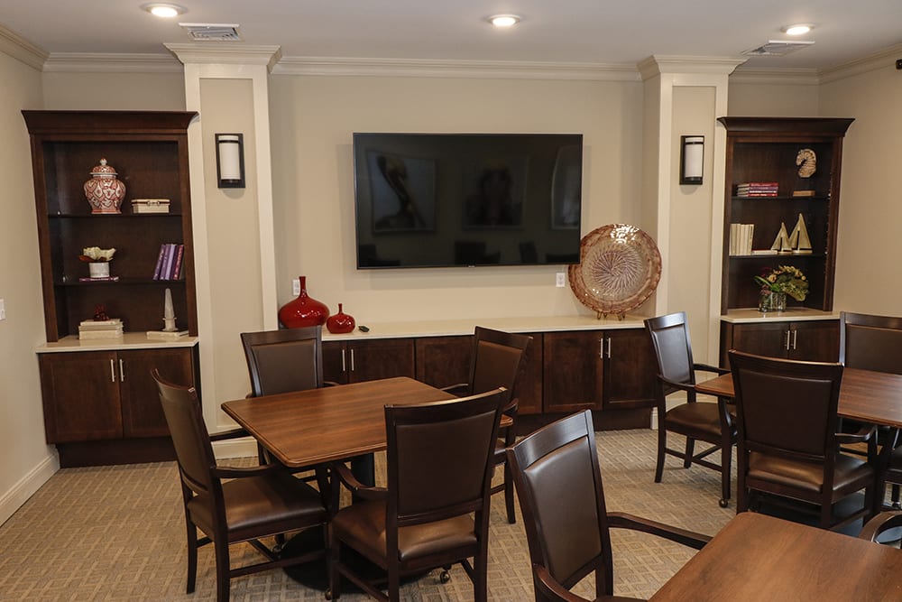 A conference room with a large TV, surrounded by tables and chairs, featuring bookshelves and decorative elements.