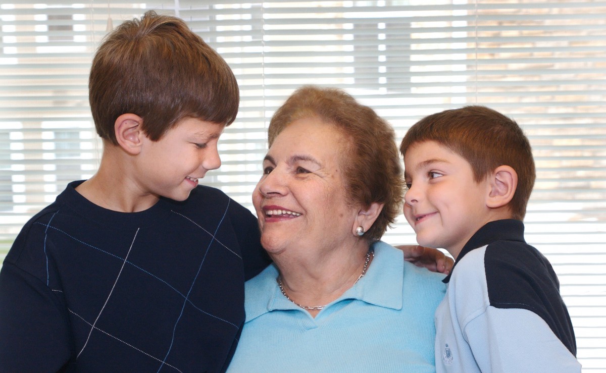 A grandmother smiling with her two grandchildren indoors.