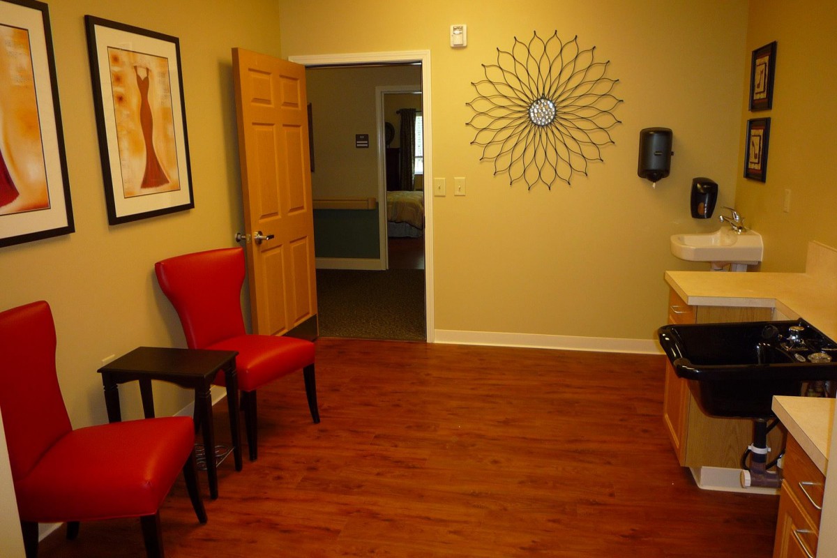 A cozy waiting room with red chairs, decorative wall art, and a hardwood floor.