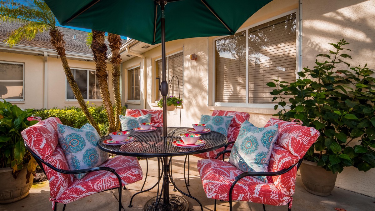 A cozy outdoor patio setup with a table, colorful cushioned chairs, and a large umbrella.