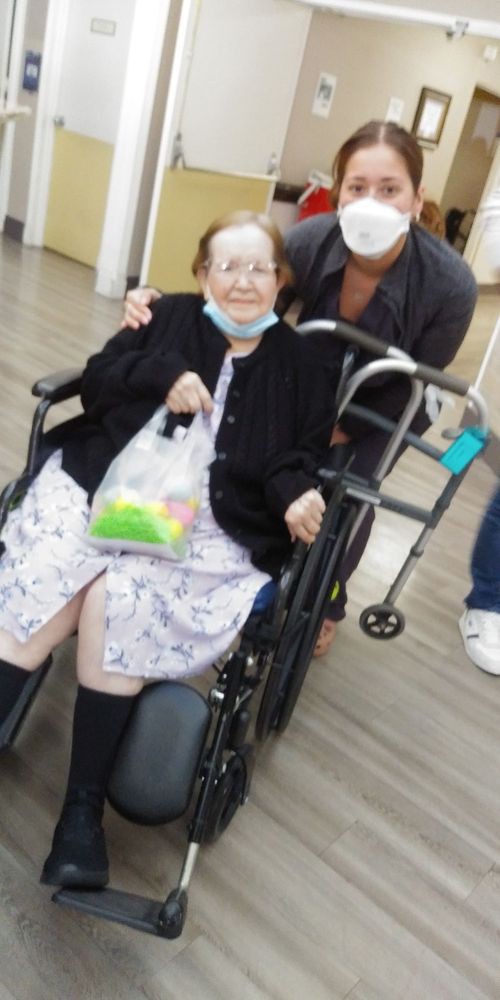 An elderly person sitting in a wheelchair, accompanied by family indoors.