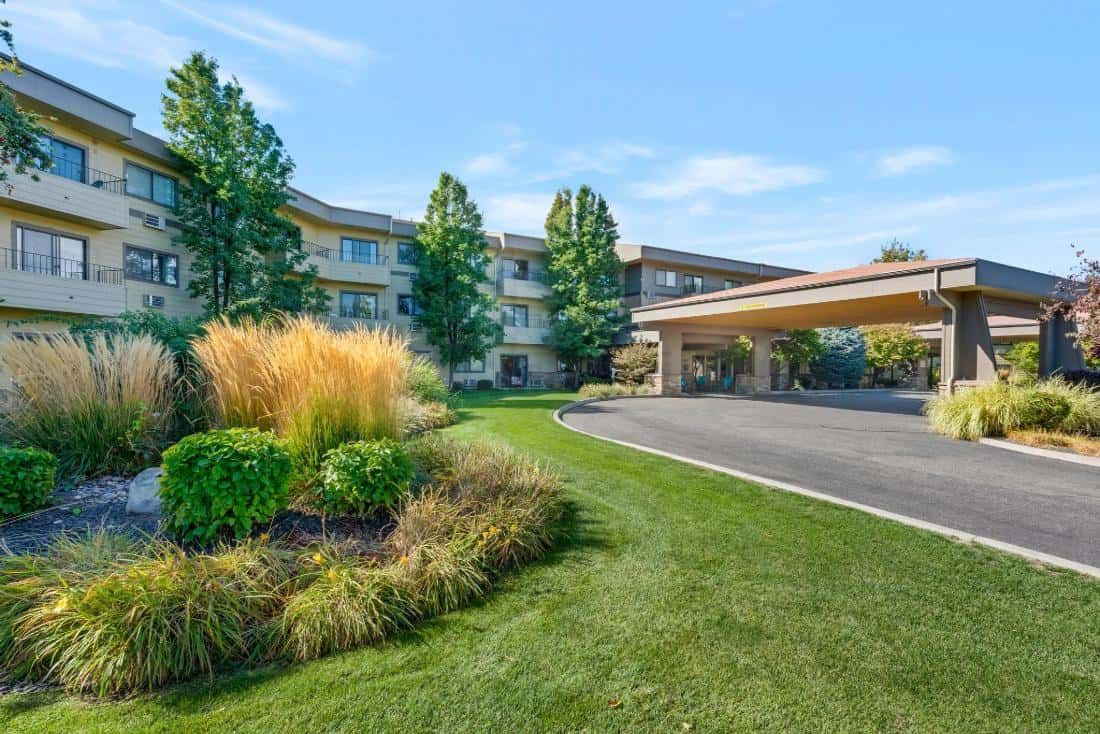 A well-manicured hotel entrance with lush greenery and a cover for vehicles.
