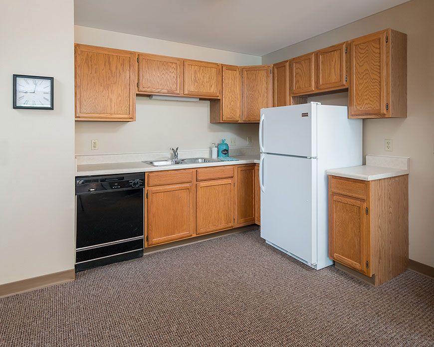 An apartment kitchen with wooden cabinets, a refrigerator, and a stove.