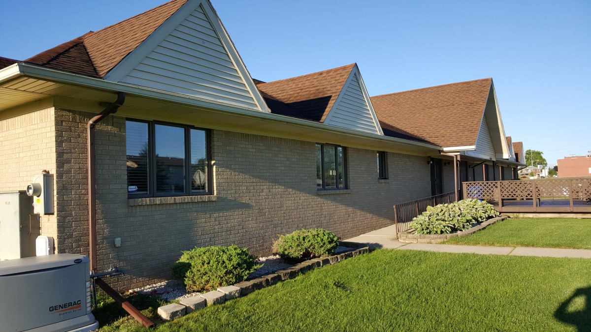 A brick residential house with a triangular roof, windows, and a neatly maintained yard.