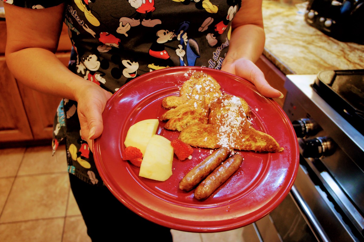 A plate of breakfast featuring French toast with powdered sugar, sausages, and sliced fruit.