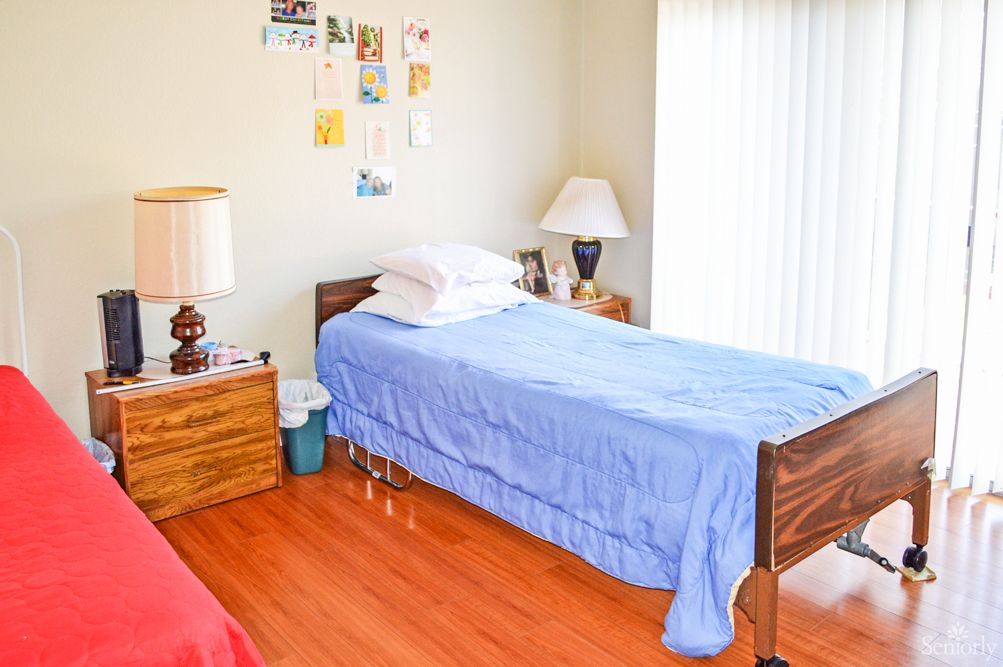 A neatly arranged bedroom with a single bed, blue bedspread, and wooden furniture.