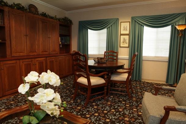 A cozy living room featuring a wooden table and chairs, decorative curtains, and a floral patterned carpet.