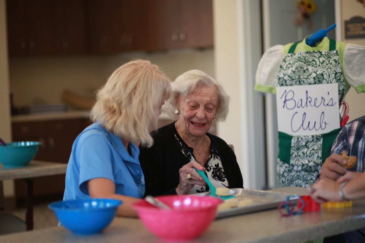Two elderly women enjoying a conversation while baking together in a kitchen.