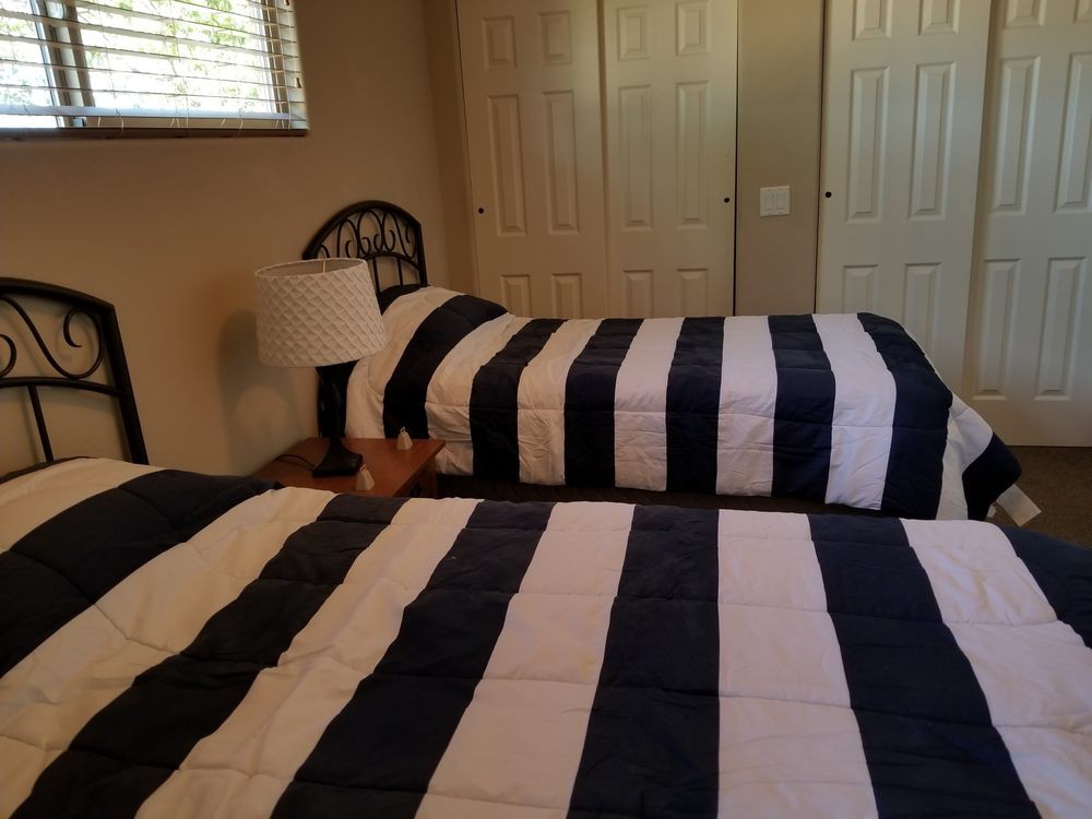 A bedroom with two single beds featuring striped bedding, a lamp, and a window with blinds.