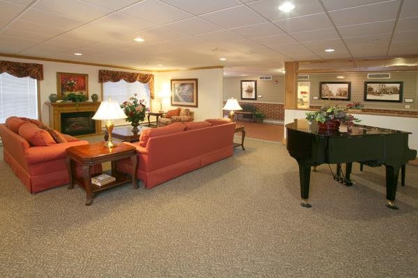 A spacious and warmly decorated living room featuring a red sofa, a black piano, and various furnishings including lamps and framed artwork.