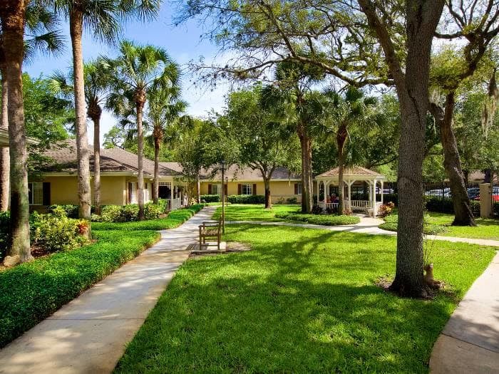 A peaceful garden scene with a walkway, lush greenery, and a gazebo under clear blue skies.