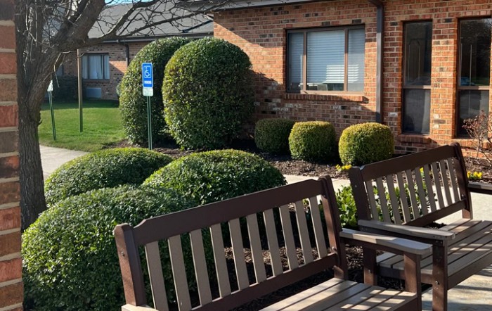 A well-maintained garden area with benches and neatly trimmed bushes in front of a brick building.