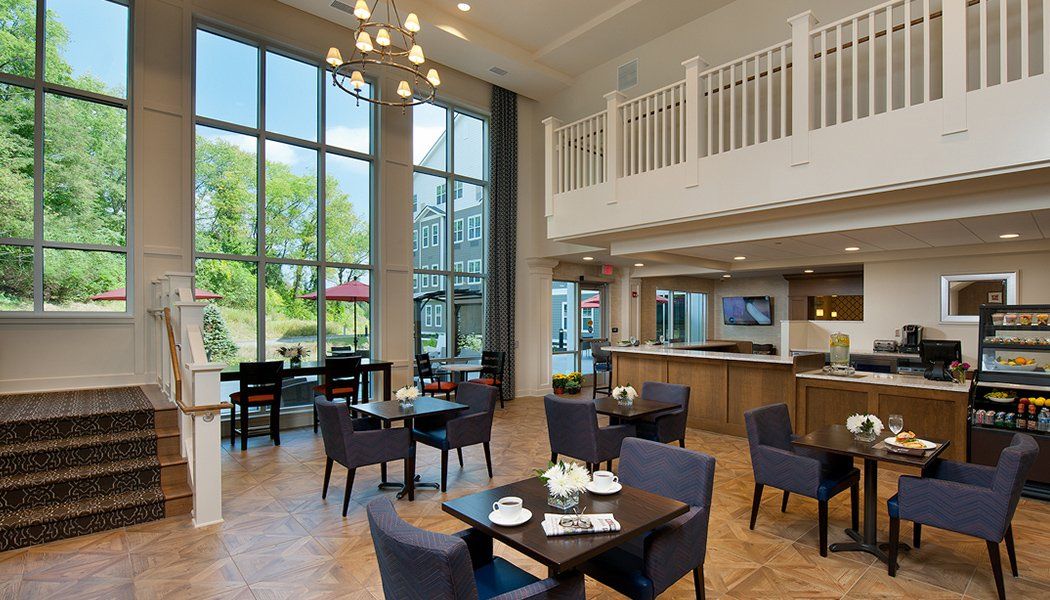 A modern restaurant dining area with large windows, offering an inviting ambiance with wooden floors and a chandelier.