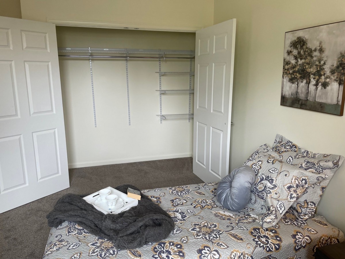 A cozy bedroom with an open closet and a patterned bedspread.