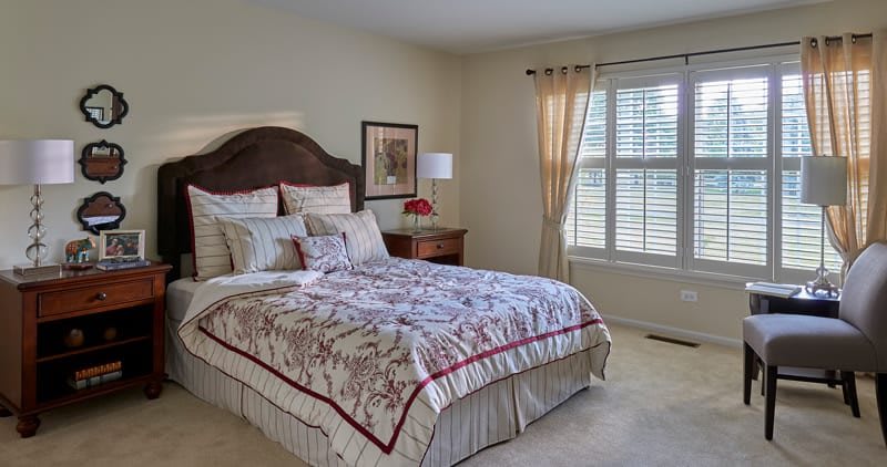 A cozy bedroom with a neatly made bed, decorative pillows, and natural light coming through the window.