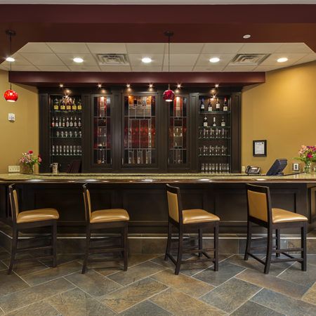 A stylish bar interior featuring a counter with high chairs and a wine rack in the background.
