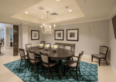 A well-appointed dining room featuring a large round table, surrounded by chairs, with a chandelier overhead and artwork on the walls.