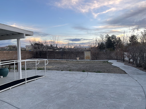 A serene outdoor space featuring a concrete patio, expansive grass area, and a beautiful sky with scattered clouds.