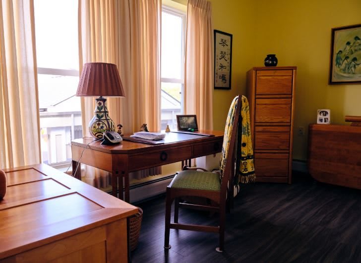 A cozy home office setup with a wooden desk and chair near a large window, complemented by a decorative lamp and warm lighting.