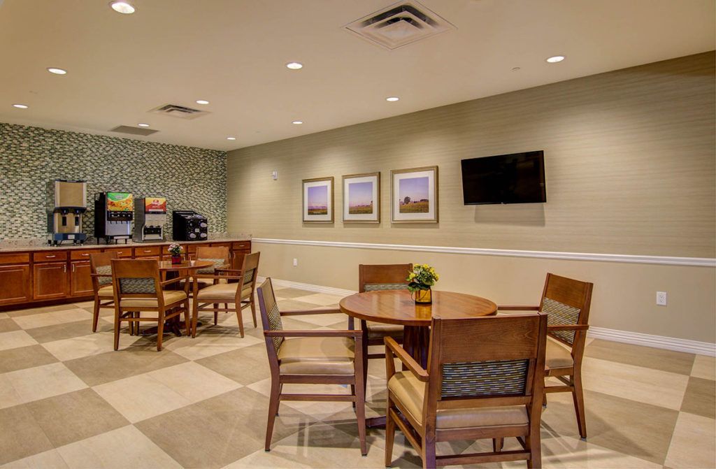 A modern lobby seating area with tables, chairs, a wall-mounted television, and decorative artwork.