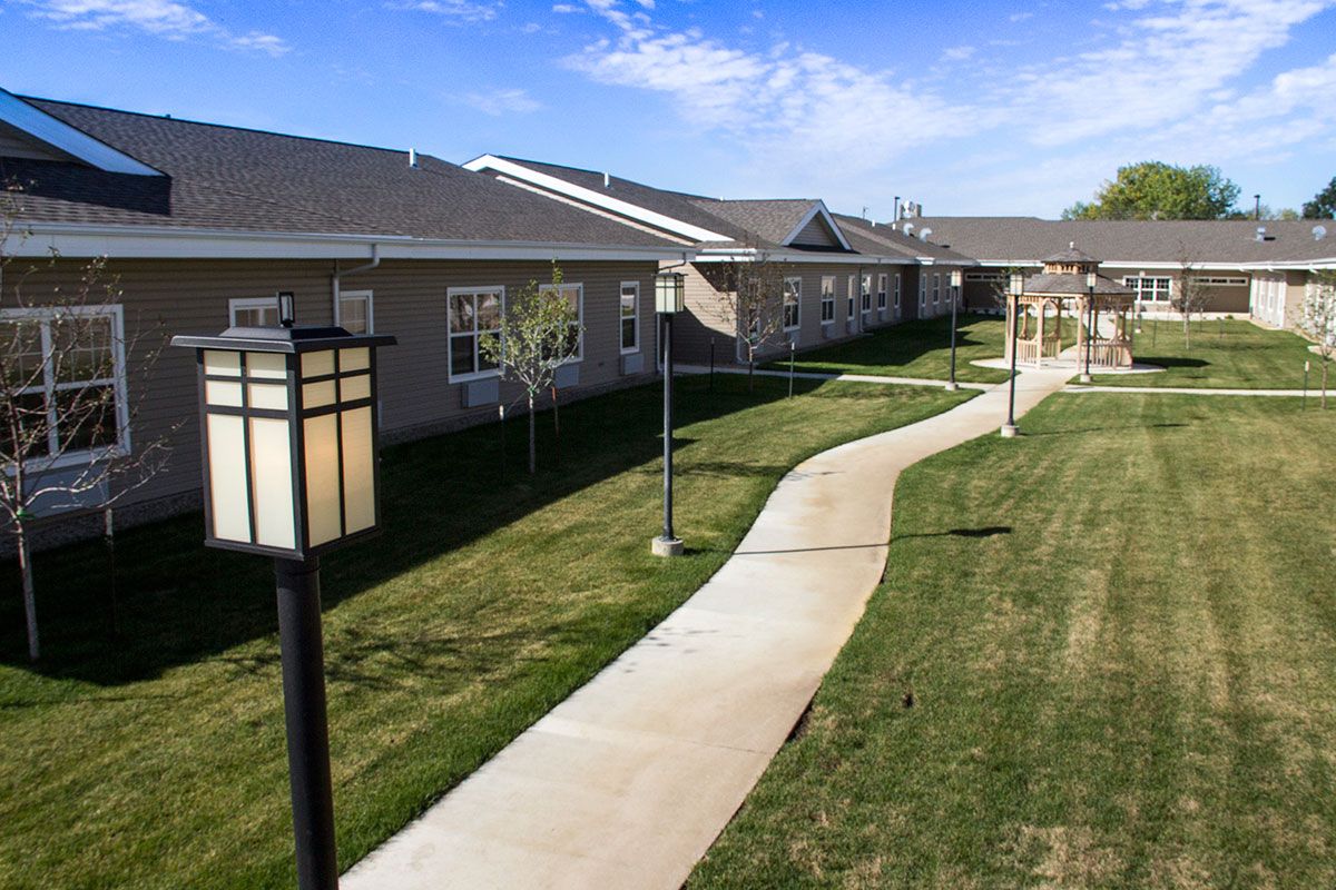 A neatly landscaped outdoor path leads to a building, with lamp posts lining the way under a clear blue sky.