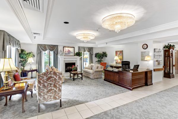 A cozy living room with traditional decor, featuring a fireplace, sofas, a desk, and chandeliers.