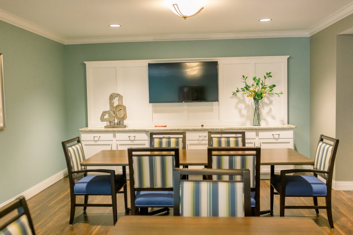 A modern dining room with striped chairs, a wall-mounted TV, and a decorative vase with flowers.