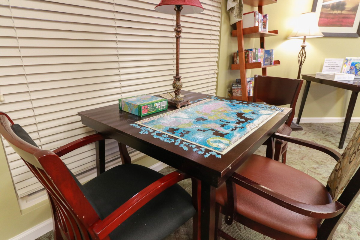 A cozy room with a puzzle in progress on the table and bookshelves in the background.